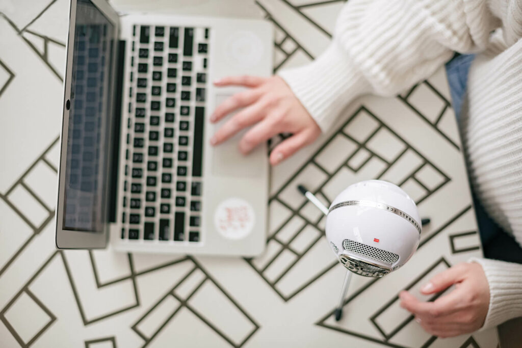 An overhead shot of co-host of The Simple & Smart SEO Show podcast and case study copywriter, Brittany Herzberg, wearing a white sweater & typing on her laptop with a podcast mic next to her. 