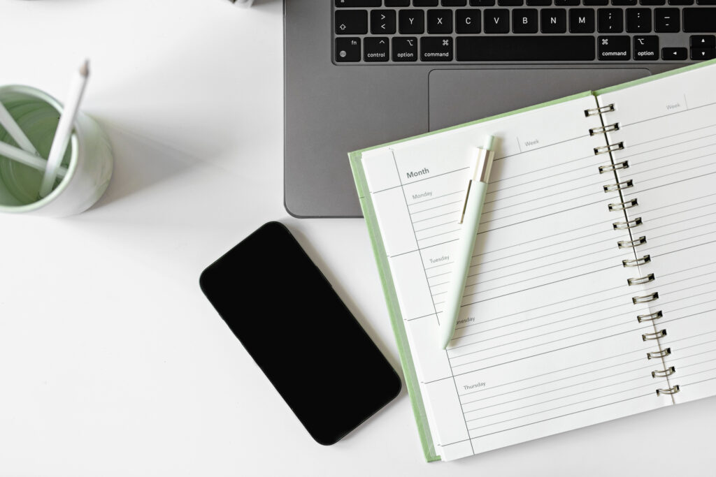 A flat-lay workspace with a laptop, smartphone, planner, and pen — representing a podcaster reviewing their content strategy and trying to figure out why their podcast isn’t growing.