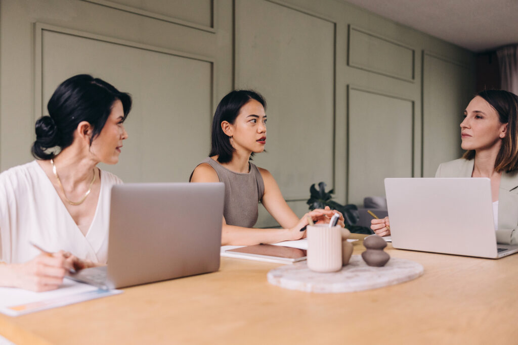 Three professionals having a strategic meeting with laptops at a conference table, representing podcast strategy and podcast growth.
