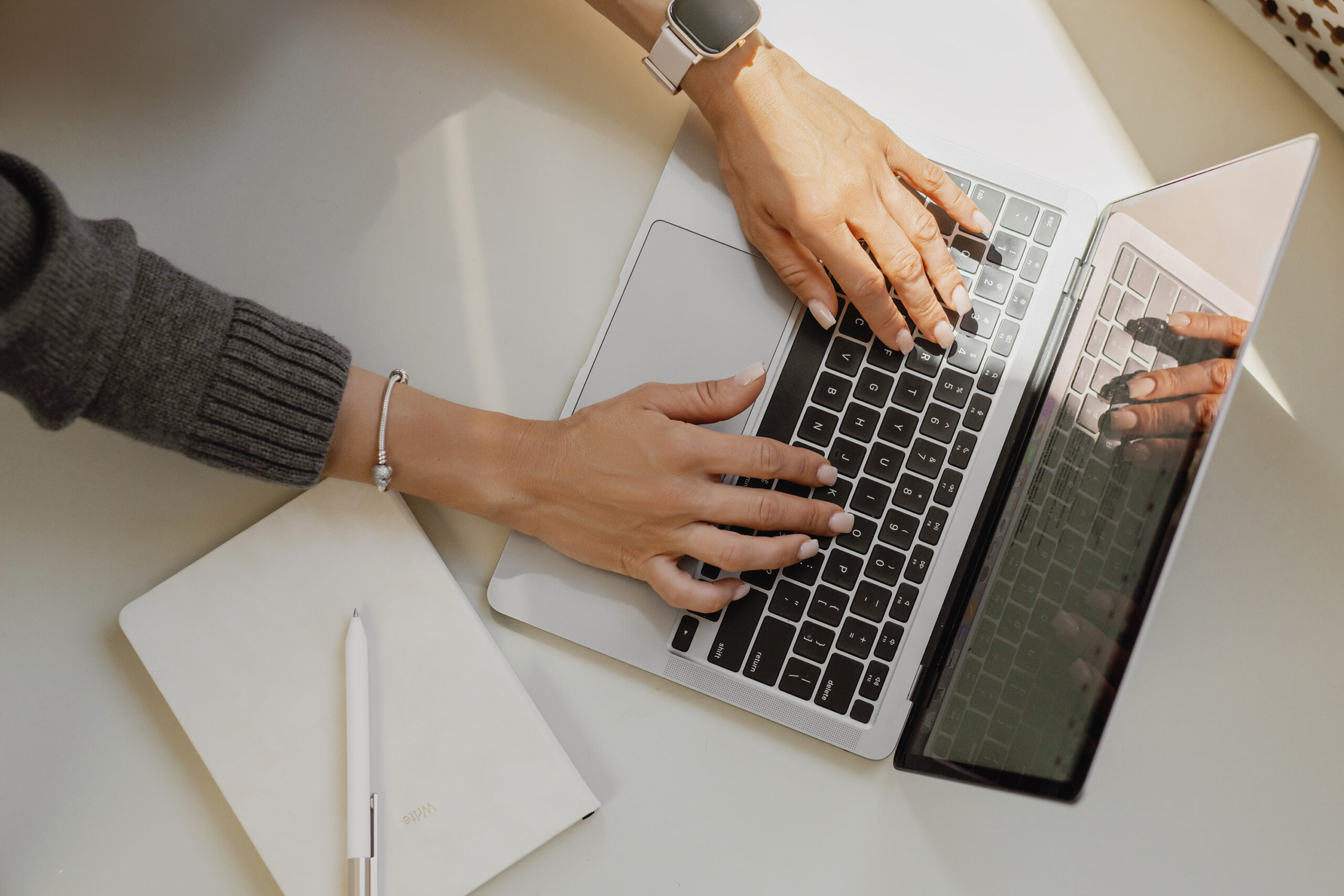 Woman's hands typing on laptop with notebook for podcast growth strategy planning and podcast visibility strategies