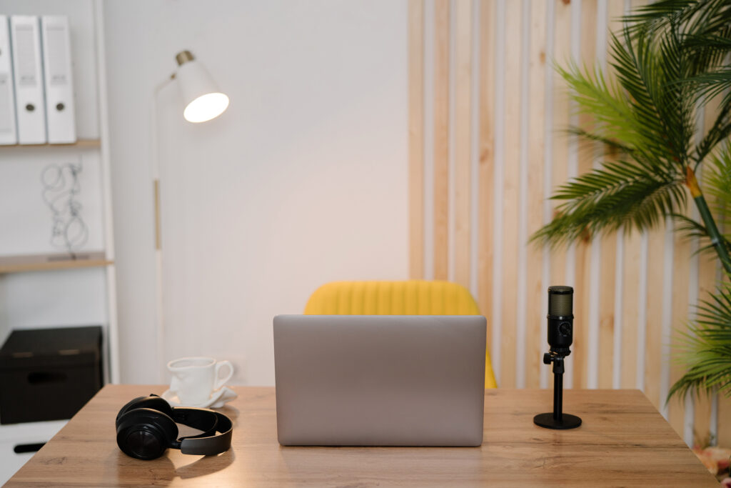 A tidy podcast recording setup featuring a laptop, headphones, and a professional microphone on a wooden desk, symbolizing the idea that your podcast is already being indexed and should be optimized to work for you. The clean, modern workspace reinforces a strategic, intentional approach to podcast content.