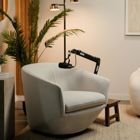 Modern podcast recording setup with a Rode microphone on an adjustable arm in front of a gray studio chair, styled with plants and warm lighting.