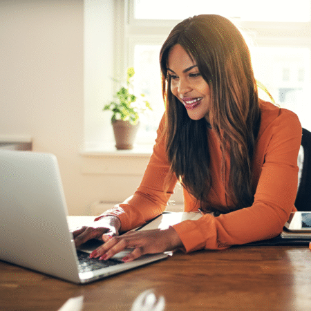 how-to-write-podcast-show-notes-that-improve-SEO Smiling woman working on a laptop at a desk, creating podcast show notes to improve podcast SEO and grow her show visibility.