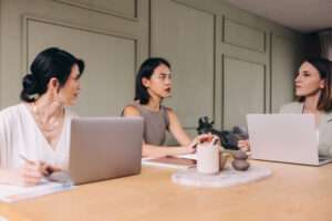 Three professionals having a strategic meeting with laptops at a conference table, representing podcast growth coaching and business strategy collaboration.