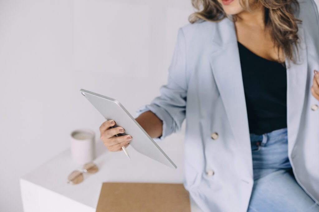 Professional woman in a light blue blazer using a tablet at a minimalist workspace, representing podcast growth strategy and business planning.