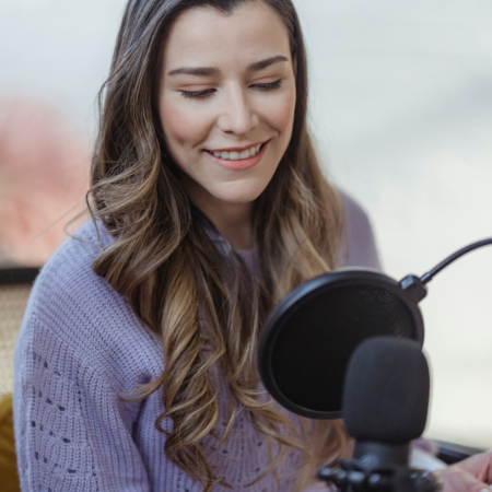 Podcaster recording How to Write Episode Titles That Get More Downloads episode at microphone in purple sweater