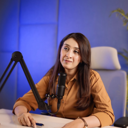 Woman recording a podcast lead generation strategy episode at a microphone in a blue studio setup