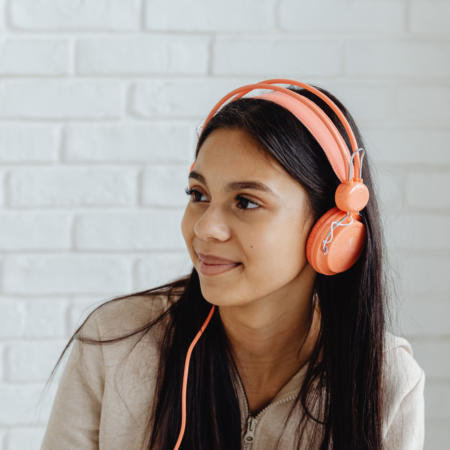 Podcast listener wearing orange headphones against a white brick background