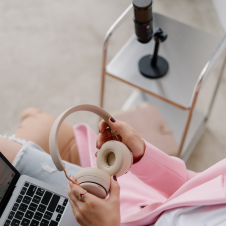 Woman holding headphones with a laptop and microphone, planning podcast episode structure for better listener retention.