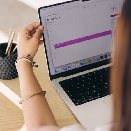 Woman reviewing her calendar on a laptop, blocking time to work on her podcast discoverability strategy.