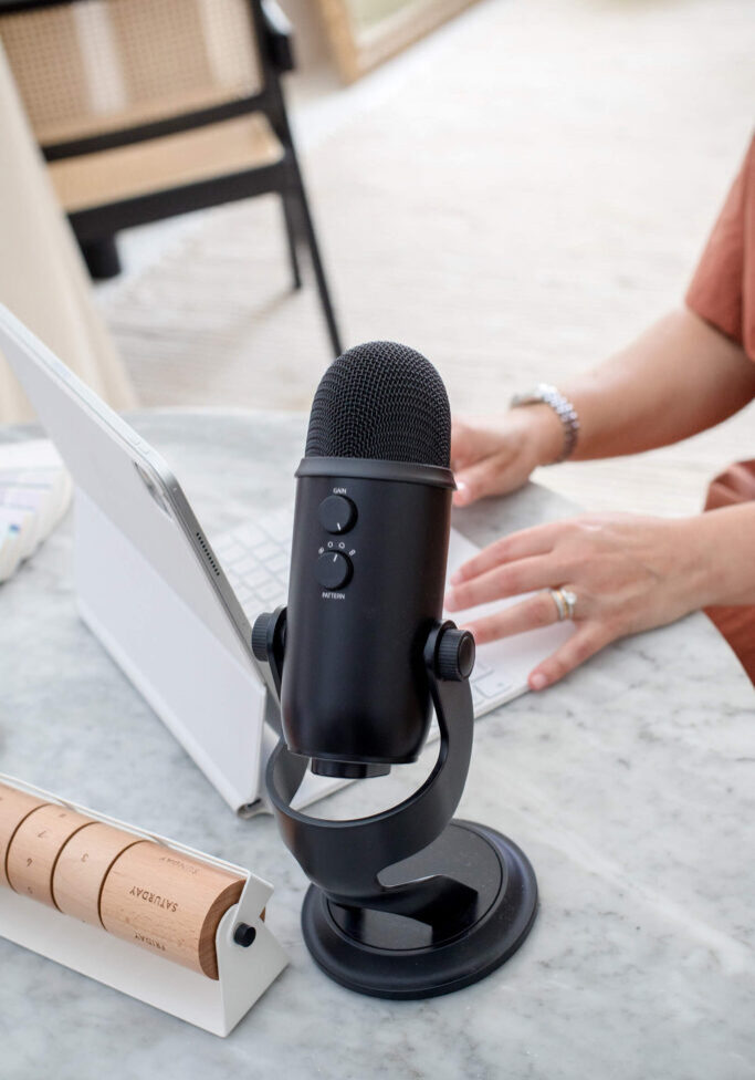 Podcast mic sitting on table while woman records on optimized podcast episode on tablet.
